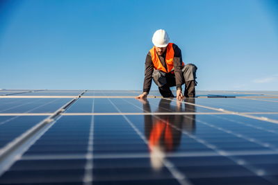 Arbeiter mit Helm an einer Photovoltaikanlage auf dem Dach